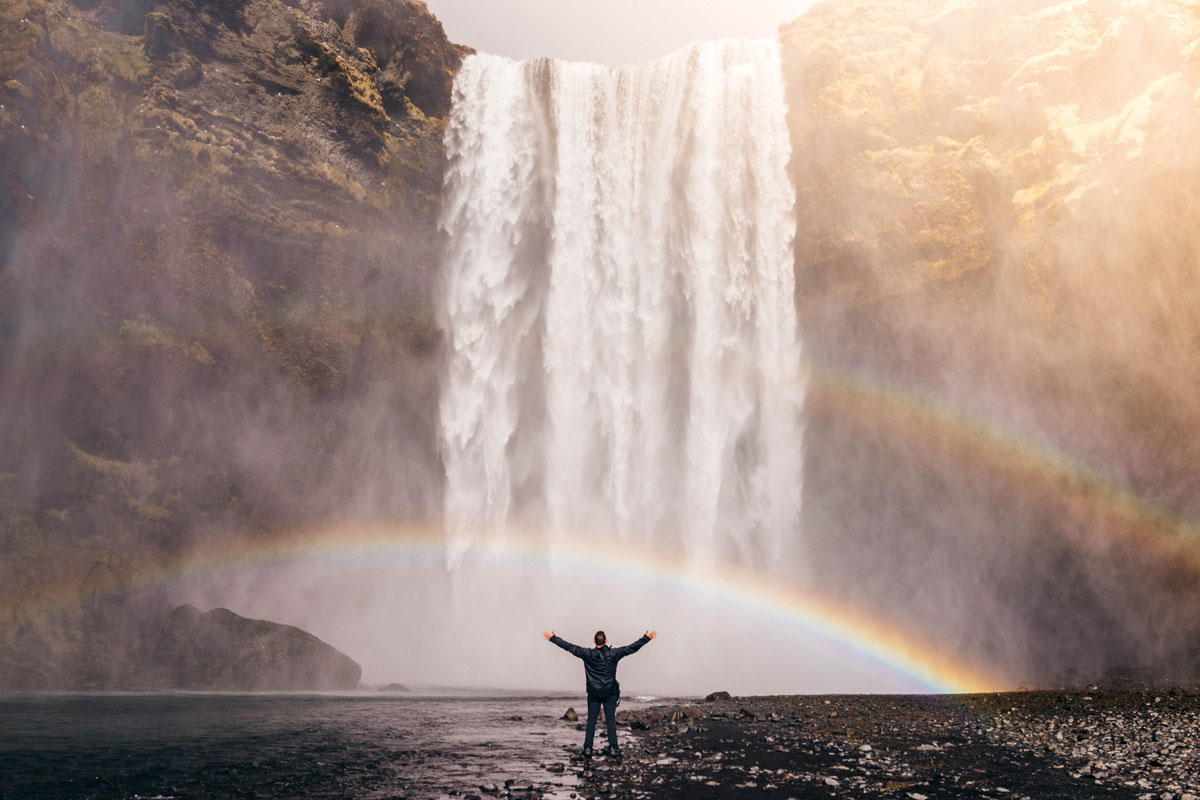 Arms raised in front of waterfall with rainbow